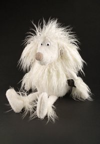 White fluffy plush dog with long shaggy fur, large beige nose, googly eyes, and floppy limbs sitting against a black background.