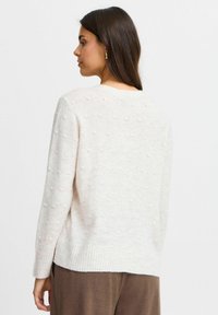 Ljusbeige tröja med en texturerad prickmönster, rund halsringning och ribbad nederkant. Har långa ärmar och en avslappnad passform.