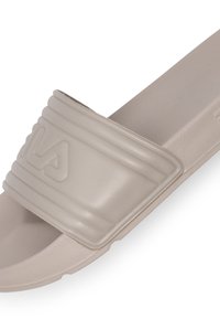 Ljusbeige halksandaler med en tjock rem som har horisontella räfflor och tryckt logotyp. Tillverkad av smidigt plastmaterial.