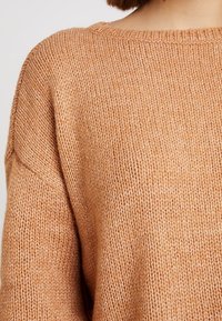 Gestrickter Pullover in sanftem, hellorangefarbenem Farbton; bietet einen lockeren Schnitt, einen weiten Ausschnitt und ein geripptes Muster, das das lässige Design betont.