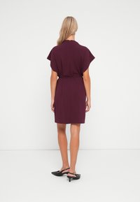 Μώβ φόρεμα με κοντά μανίκια, ζώνη στη μέση, μήκους μέχρι το γόνατο και λεία υφή, σε συνδυασμό με μαύρες μυτερές γόβες.