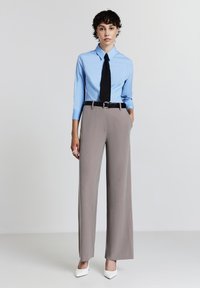 Camicia a maniche lunghe azzurro chiaro con colletto, abbinata a pantaloni larghi beige a vita alta e una cintura nera, completata da tacchi bianchi.