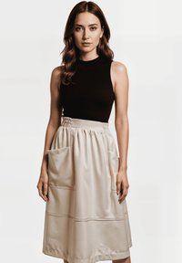 Top negro sin mangas combinado con una falda crema hasta la rodilla que presenta grandes bolsillos laterales y detalles de costura horizontal.