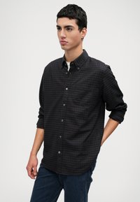 Fekete és lila kockás ing gallérral, mellzsebbel és felgöngyölt ujjal, sötétkék nadrággal párosítva.