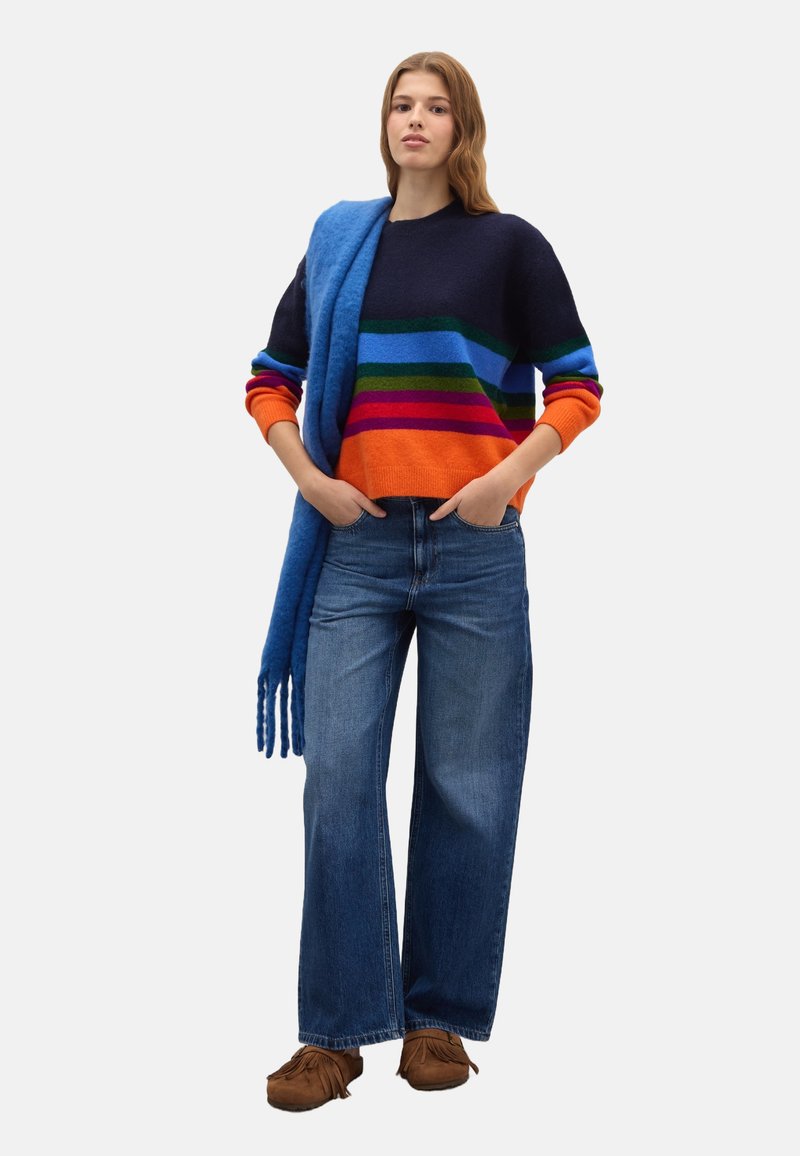 Striped sweater in navy, orange, and green; relaxed fit. Paired with wide-leg jeans and a blue scarf. Soft texture, casual style.