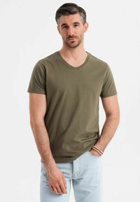 T-shirt verde oliva con scollo a V realizzata in morbido cotone, con maniche corte e una vestibilità rilassata. Indossata con jeans azzurri chiari e braccialetti.
