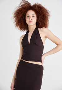 Melnā haltera tipa cropped tops, izgatavots no gluda auduma, ar savilkta bodice un pieguļošu dizainu, apvienots ar atbilstošu melnu svārku.