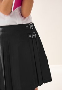 Zwarte geplisseerde rok met zilveren gespaccenten en banden in de taille. Gemaakt van een gladde stof, met nette, gestructureerde plooien.