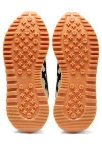 Podešve bot s oranžovou gumou, texturovaný vzor s hvězdami a drážkami, kontrastující černý a krémový vršek viditelný na okrajích.