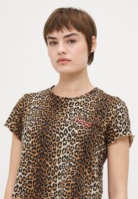 Tricou cu imprimeu leopard, cu mâneci scurte, gât rond și o textură moale. Prezintă culori negre, maro și crem, cu un detaliu brodat.