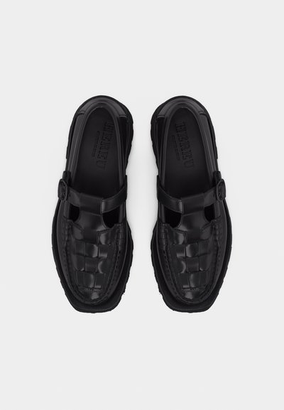 Paire de mocassins en cuir noir avec détails tissés et brides à boucle, vus de dessus sur un fond blanc.