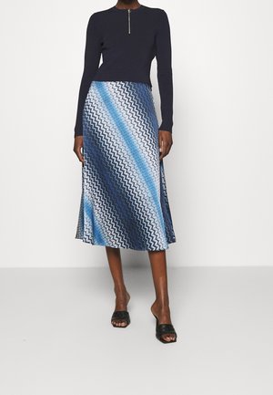 Haut en maille marine avec une encolure zippée, assorti à une jupe midi bleue à motifs présentant un design en zigzag dans des nuances dégradées de bleu et de blanc.