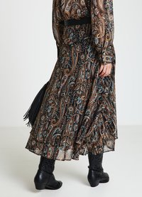 Jupe longue à volants avec un motif cachemire dans des tons marron, bleu et noir. Accessoirisée d'une ceinture noire et associée à des bottes noires montant jusqu'aux genoux.