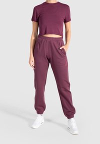 T-shirt courte bordeaux et jogging assorti en tissu doux. Le jogging possède une taille élastique et des poches latérales. Des baskets blanches complètent le look.