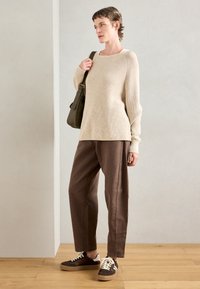 Beige ribbad stickad tröja, bruna löst sittande byxor och bruna sneakers med vita detaljer. Håller en olivgrön axelväska.