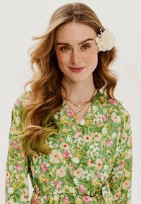 Kvetinové áčkové šaty s zeleným podkladom a ružovými, bielymi a žltými kvetmi. Hladká látka, dlhé rukávy a priliehavý pás s viazaním.