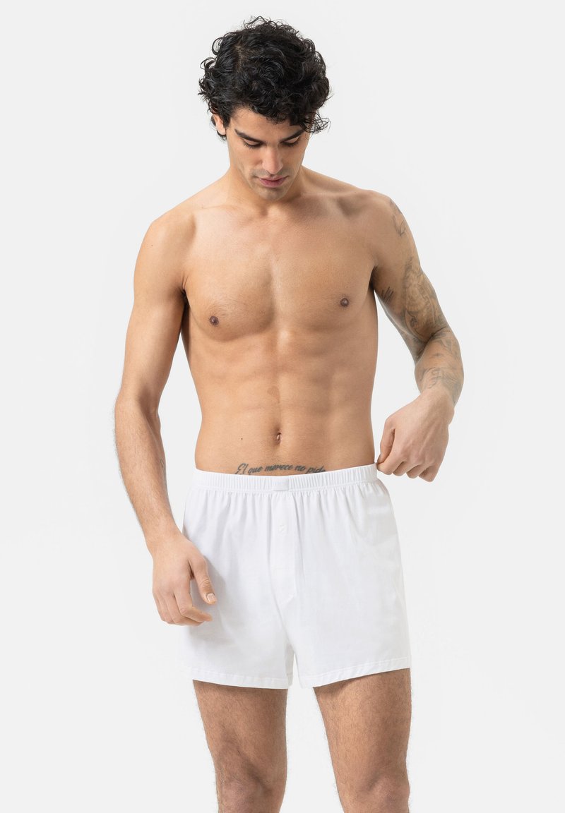 Boxers en coton blanc avec une ceinture élastique. Texture douce, coupe ample et un bouton unique à l'avant.