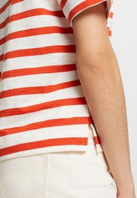 Camisa de manga corta a rayas en blanco y naranja. Fabricada en tejido ligero, presenta un dobladillo ligeramente redondeado con aberturas laterales.