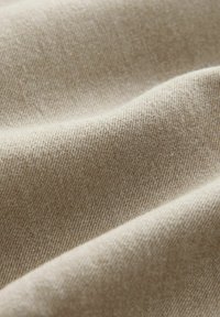 Tissu beige avec une surface lisse et texturée, présentant de fins motifs de tissage diagonal et des couches douces et pliées.