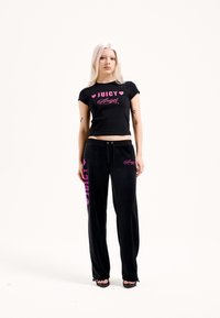 Fekete rövidített póló rózsaszín "JUICY" és "Angel" feliratokkal, fekete velúr nadrággal, melyen rózsaszín részletek és oldalán logó található.