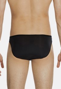 Slip da bagno neri con una texture liscia, design a vita bassa e copertura minima. Presentano un colore uniforme e una vita elastica.