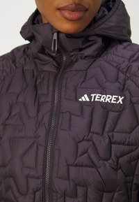 Polstret jakke i mørkeblå med lynlåslukning, hætte og geometrisk quiltet mønster. Har "TERREX" logo i hvidt på brystet.