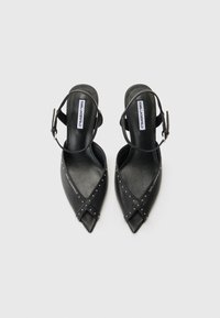 Zwarte hoge hakken sandalen met een spitse neus, gemaakt van leer, met een kruislings ontwerp met zilveren studs en een enkelbandje.