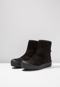 Bottes noires en daim à la cheville avec une semelle en caoutchouc texturée, un dessus lisse et une languette à l'arrière pour un enfilage facile.