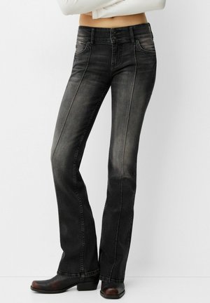 Schwarze Jeans aus Denim mit einem ausgestellten Bein-Design, zwei Knopfverschluss und detaillierten Fronttaschen. Dezente Ausbleichung mit einer glatten Textur.