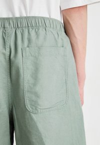 Shorts verzi din in, cu talie elastică, un singur buzunar posterior tip aplicat și o textură netedă.