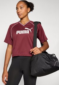 Maroon cropped athletic shirt with white PUMA logo, short sleeves, paired with black leggings and a black duffel bag with a shoulder strap.