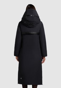 Pikk must voodriga mantel suure kapuutsiga, millel on läikiv logo seljal ja elastne vöö, millel on reljeefne kiri. Sile tekstuur.