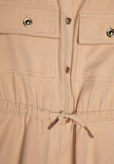 Μπεζ φόρεμα πουκάμισου με εφαρμοστή μέση, δύο μπροστινές τσέπες με χρυσά κουμπιά και κορδόνι για ρυθμιζόμενη εφαρμογή.