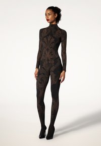 Sort tætsiddende bodystocking med et struktureret gyldent blomstermønster, høj halsudskæring, lange ærmer og en glat overflade. Båret med sorte stiletter.