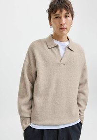 Lys beige strikket sweater med krave og en let V-hals. Har lange ærmer, ribbede manchetter og en blød tekstur. Laget over en hvid skjorte.