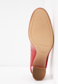 Chaussure en cuir verni rouge avec un design épuré, bout pointu et semelle en caoutchouc texturée beige. Présente un logo et une indication de taille.