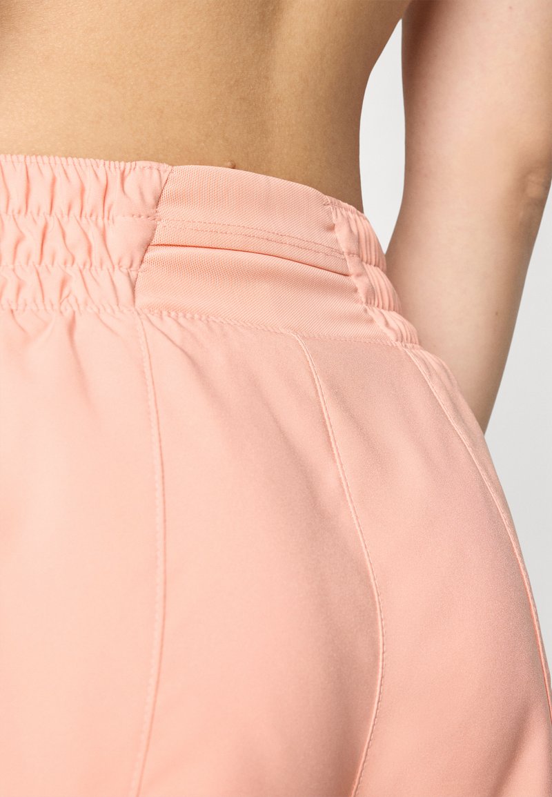 Los pantalones rosa claro presentan una cinturilla elástica fruncida, una textura suave y detalles de costura sutiles a lo largo de los lados.