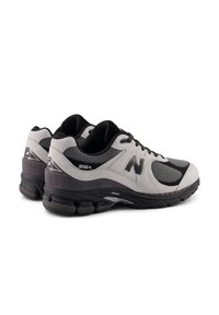 Paire de baskets New Balance 2002R grises et noires avec des détails en mesh et cuir, lacets noirs et semelles rembourrées, vues de dos.