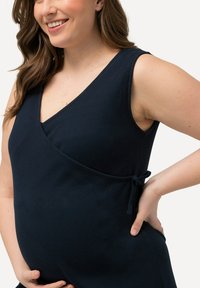 Granatowa sukienka w stylu wrap z głębokim dekoltem w kształcie V, bez rękawów, prążkowaną teksturą i wiązaniem z boku, które podkreśla krągłości.