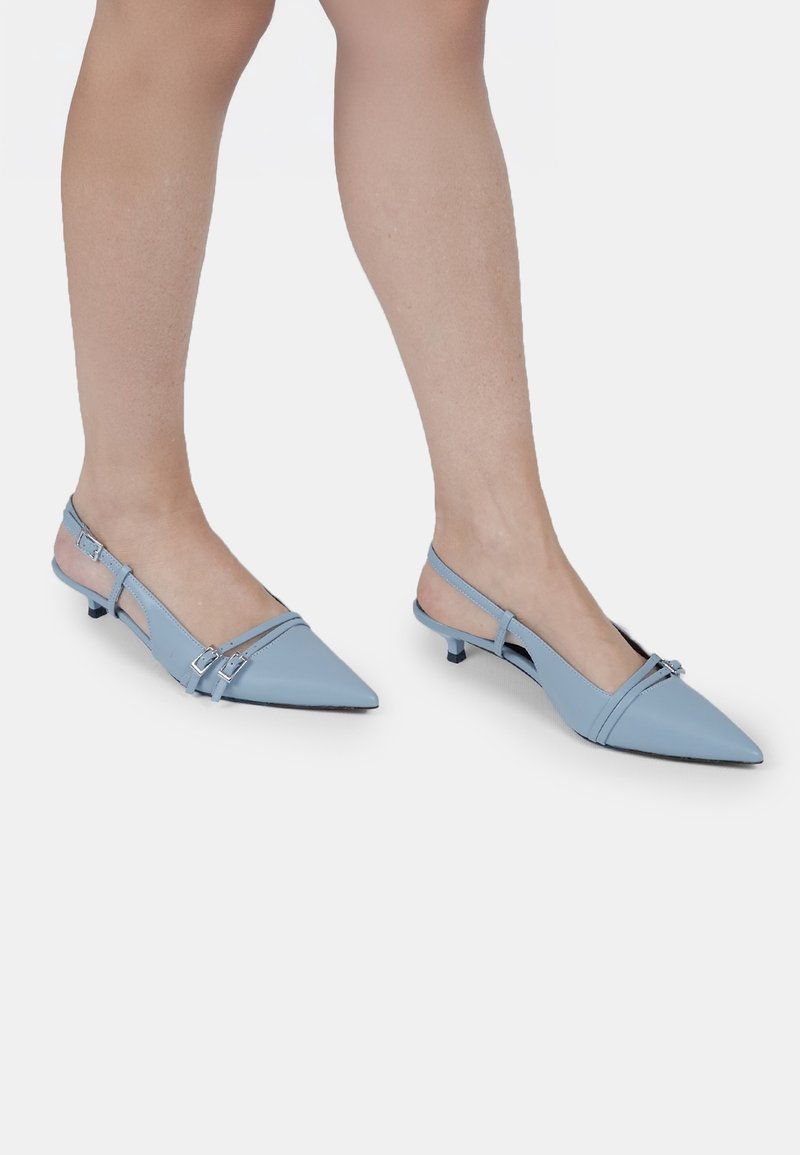 Escarpins slingback bleu clair avec un bout pointu, des brides fines, des détails en boucle argentée et un petit talon aiguille. Texture en cuir lisse.