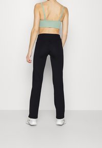 Leggings noirs à taille haute, associés à un brassière vert clair. Le matériau semble lisse, avec des coutures peu visibles.