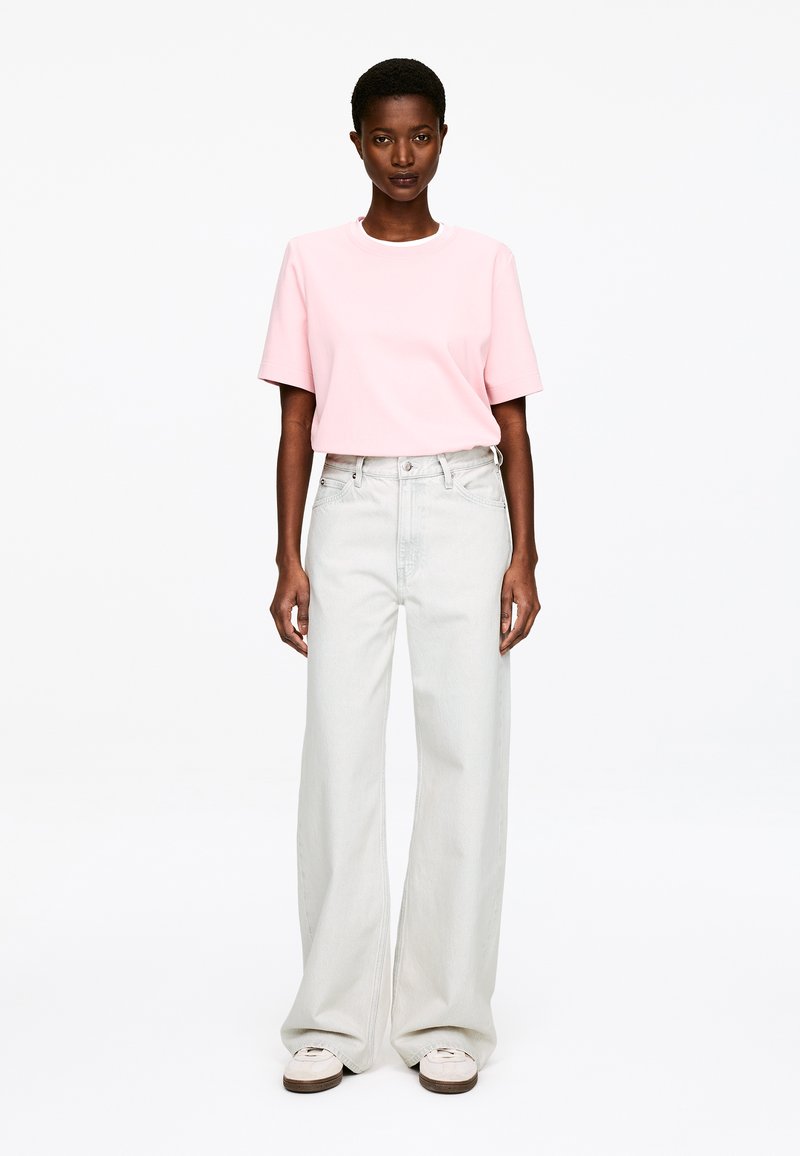 T-shirt en coton rose clair à manches courtes, associée à un pantalon large en denim pâle taille haute et des baskets blanches. Coupe simple et décontractée.