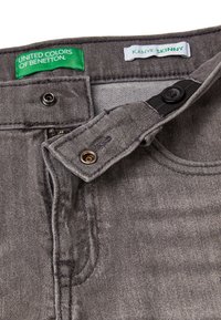 Jeans de denim gris con un ajuste slim, con cierre de botón y cremallera, y etiquetas de 'United Colors of Benetton' y 'Kanye Skinny'.