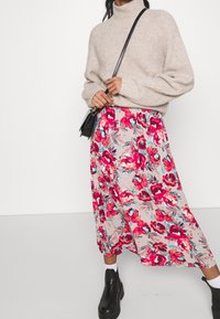 Beige ribbed sweater paired with a pink floral midi skirt featuring red and turquoise flowers, worn with black chunky boots and white socks.