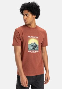 Rust-colored cotton t-shirt with a crew neck, featuring a mountain graphic and text "Feel the Outside Heal the Inside," short sleeves.