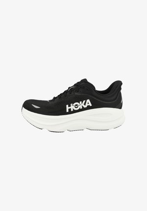 Czarne buty do biegania z siateczkową cholewką, grubą białą podeszwą środkową i czarną podeszwą zewnętrzną. Posiadają wyróżniające się logo HOKA po boku. Związane sznurowadłami.