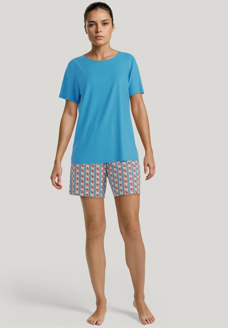 Blauw kortmouw shirt gecombineerd met gebloemde shorts met witte en rode strepen. Stevige stof; comfortabele pasvorm.