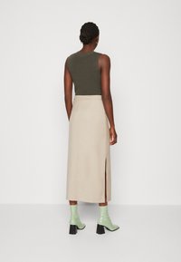 Grön ribbad linne, beige maxikjol med en sidosplit, och blanka gröna klackboots. Slät tyg med figurnära design detaljer.