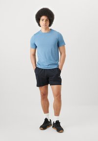 Lys blå atletisk t-skjorte, korte ermer, kombinert med svarte shorts. Svarte joggesko med gummisåler, hvite ankelsokker. Enkelt design, ingen synlige mønstre.