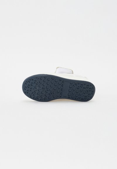 White shoe with a textured blue rubber sole, featuring a honeycomb pattern and smooth upper material. Minimalist design with clean lines.